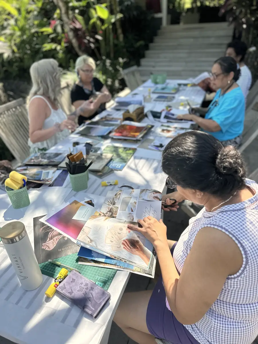 A woman cutting images from magazines at the long collage table during Ana's retreat in Bali